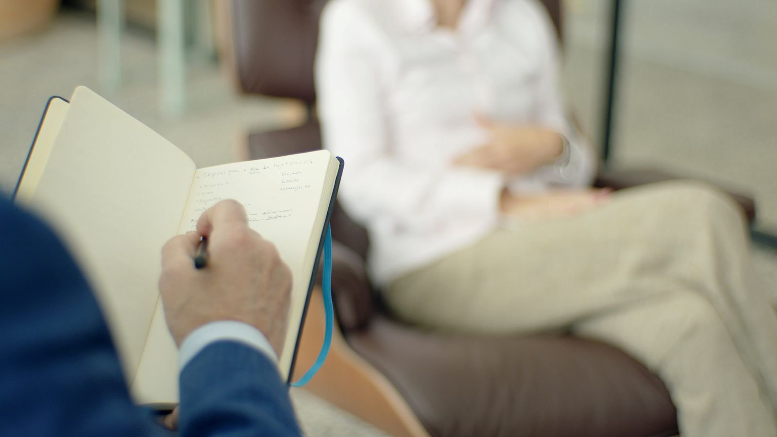 An adult writing notes in a notebook at a desk