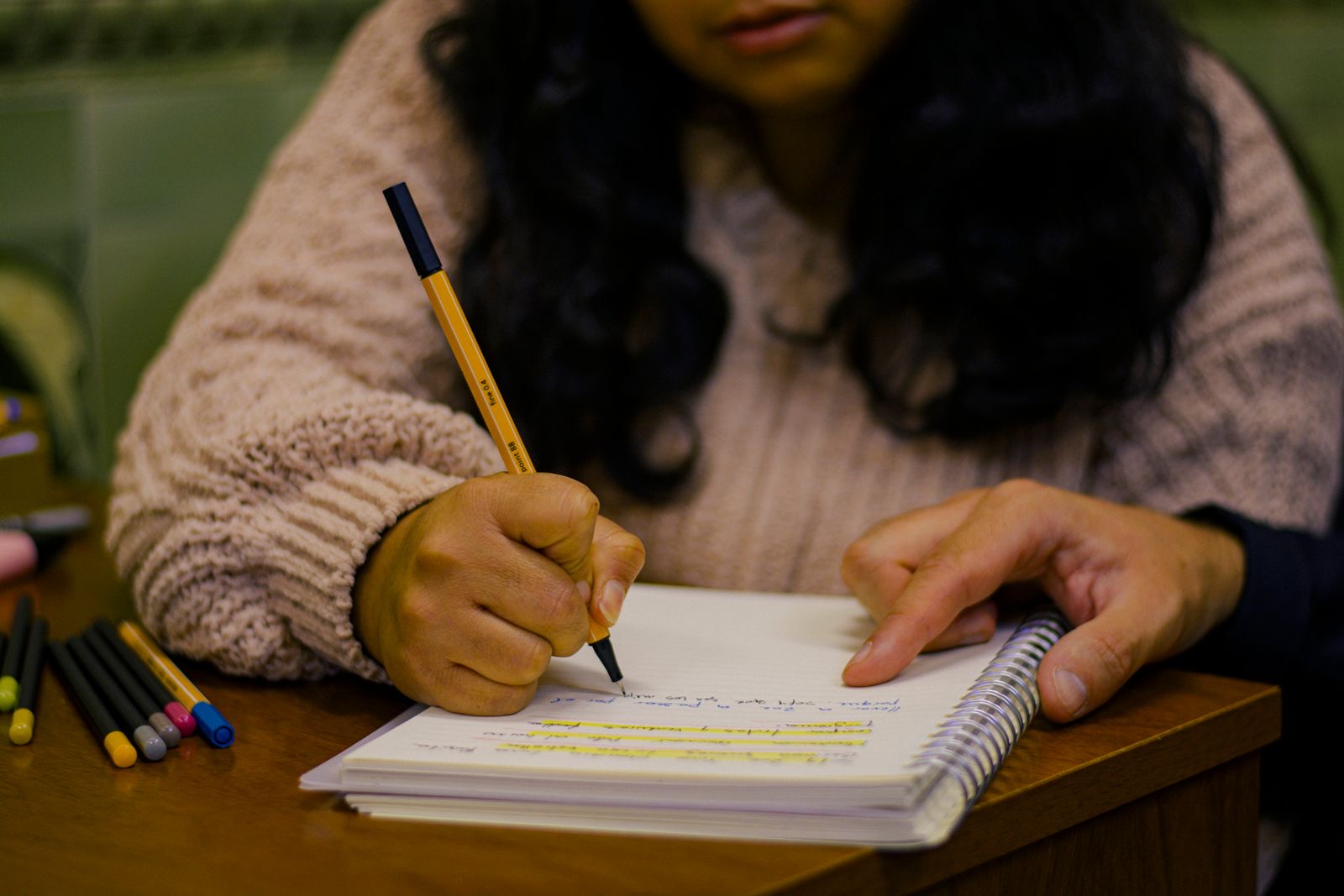 A young person writing in a notebook with a yellow pen